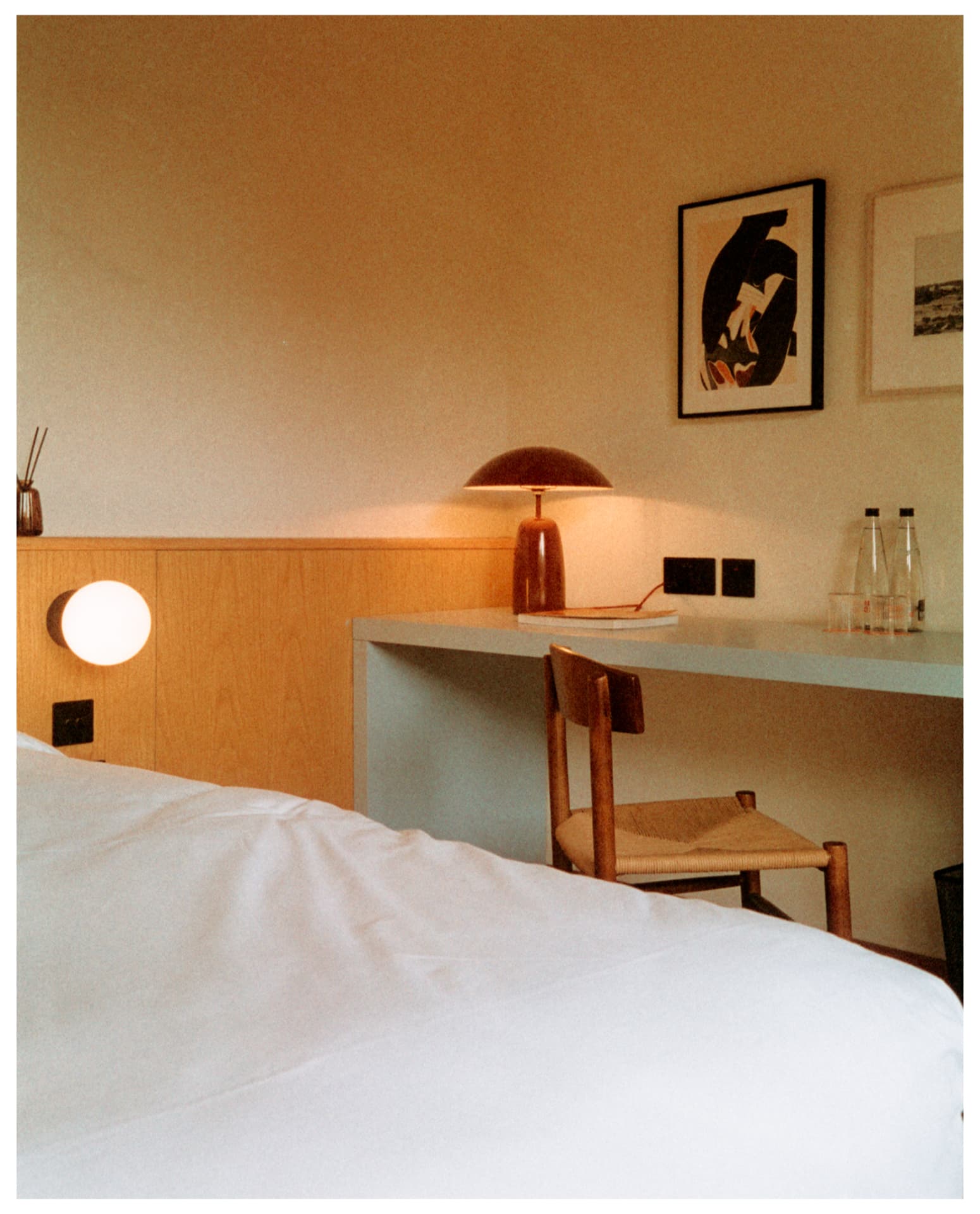 Bedroom with oak headboard, globe wall light and desk lamp, shot on film