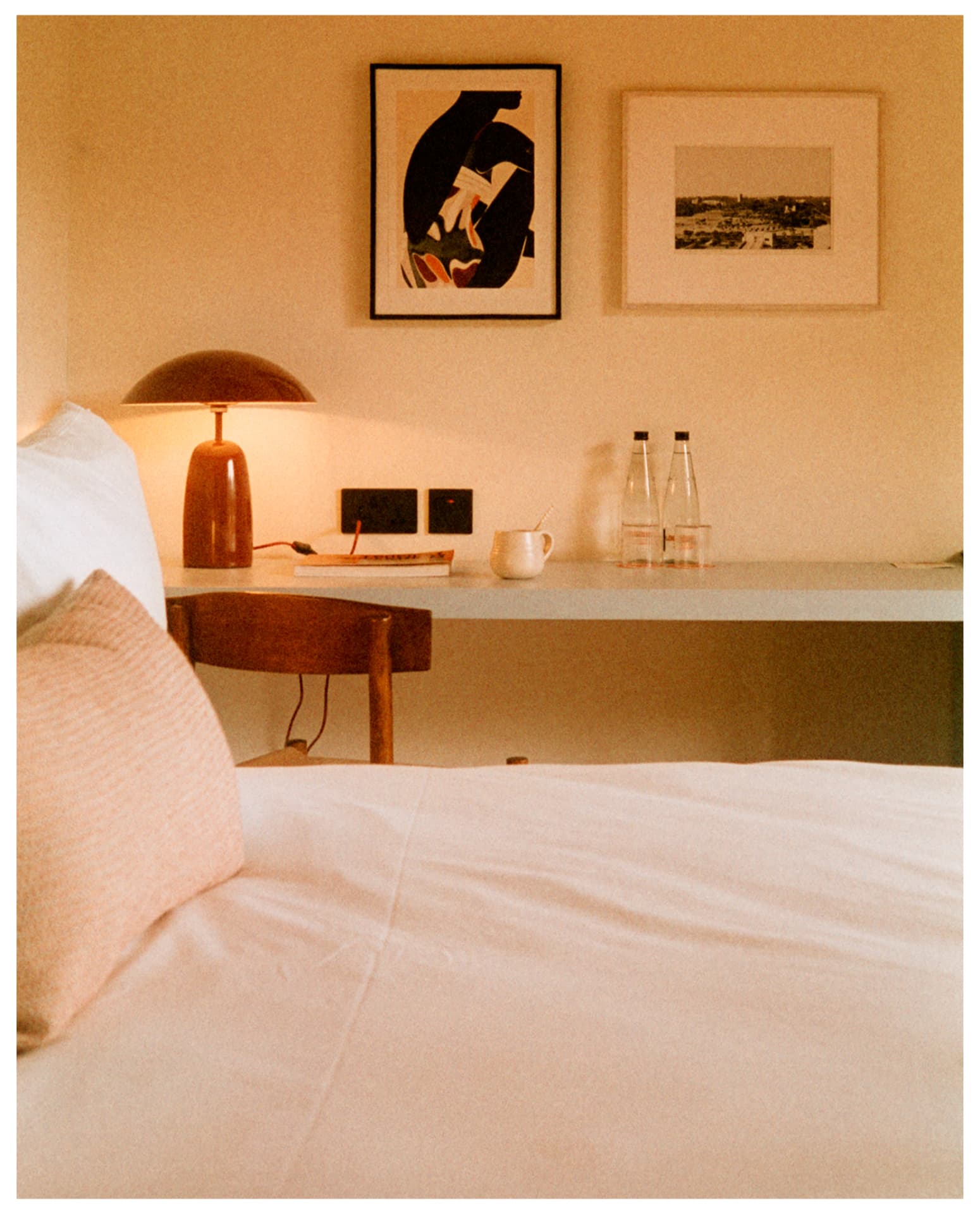Warm bedside detail with lamp, framed art and glass bottles, shot on film