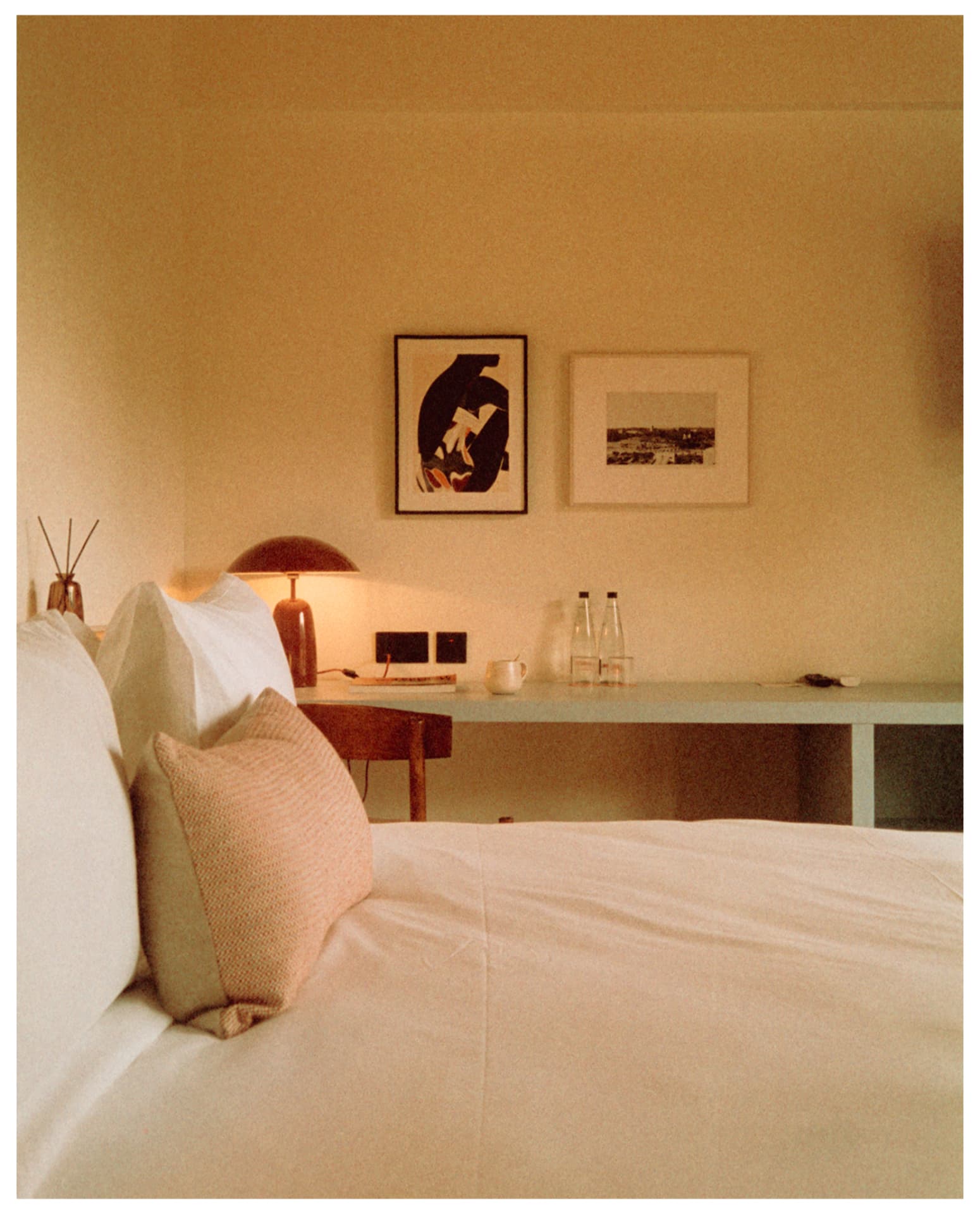 Made bed with cushions facing a desk and framed prints, shot on film